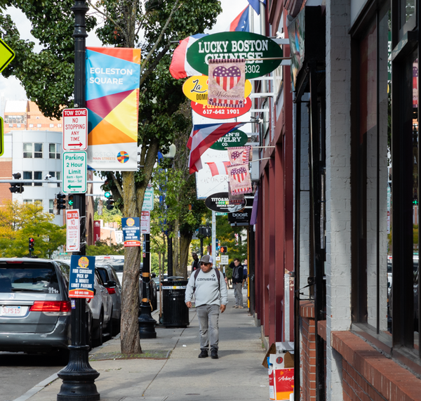 Man walks down Egleston square sidewalk below flag and business signs